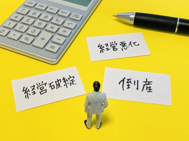 経営破綻・経営悪化・倒産の文字、人の模型、電卓、ペン